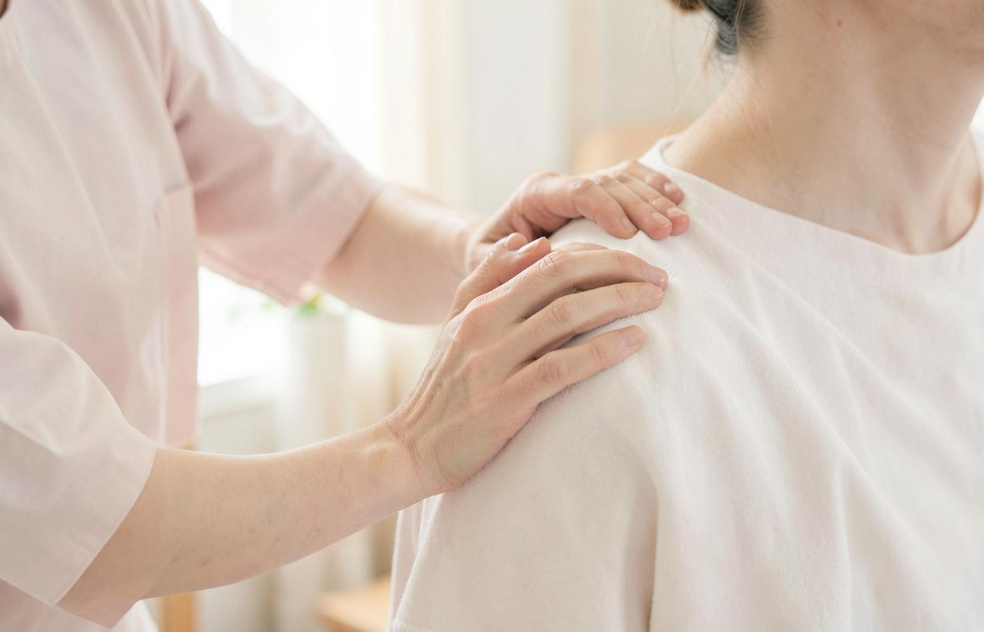 A practitioner's hands resting supportively on a client's shoulder in a calm therapy room